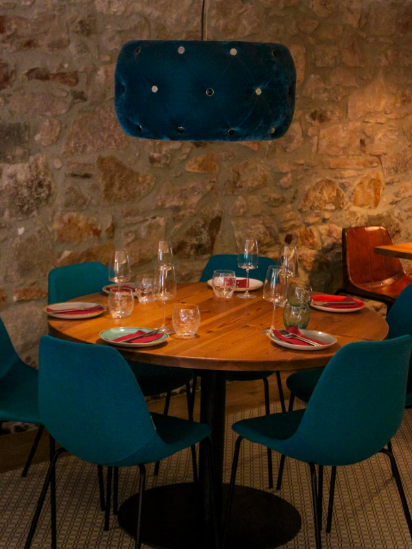 Round table with turquoise chairs under velvet lamp on stone wall